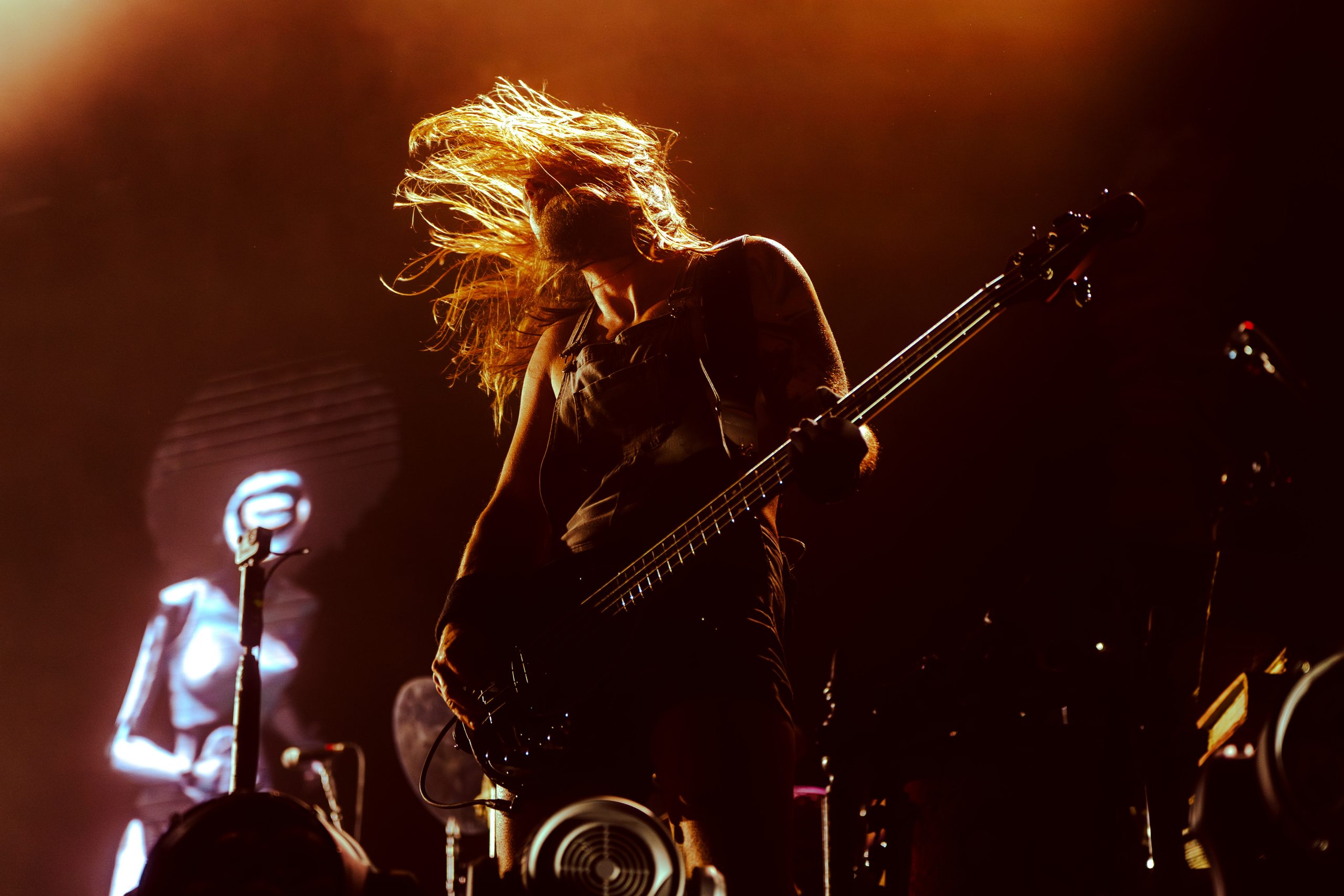Musicien sur scène jouant de la basse, cheveux au vent, éclairé par une lumière orange intense lors d’un concert au Foreztival.