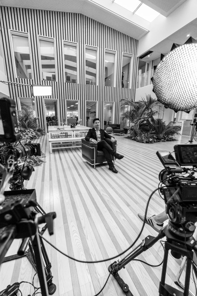Tournage d’une interview, avec deux caméras et un éclairage, dans un grand hall intérieur d'une entreprise.
