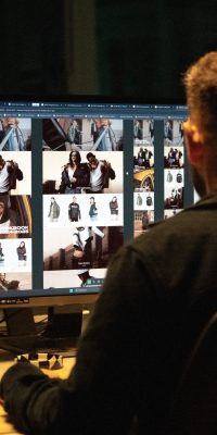 Personne de dos travaillant sur un ordinateur, écran affichant la mise en page d’un site e-commerce/lookbook.