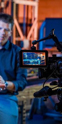 Tournage d'une interview avec caméra filmant un homme assis dans un atelier industriel.