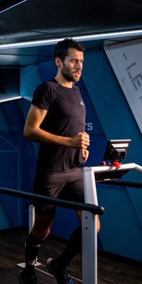 Athlète courant sur un tapis de course dans un laboratoire de performance, éclairé par une softbox.