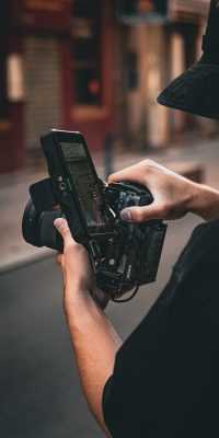 Cadreur tenant une caméra et réglant l’écran de contrôle pendant un tournage en extérieur.
