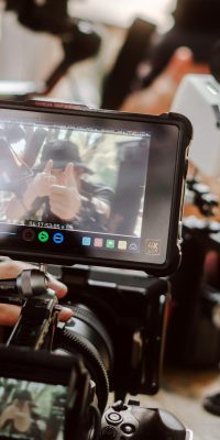 Gros plan sur un moniteur de caméra affichant une personne faisant un signe “pouce levé”, entouré de matériel de tournage.