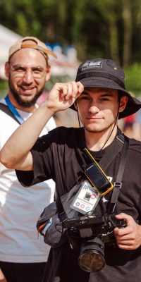 Deux membres de l’équipe vidéo dont l'un tient une caméra sur le site de festival en plein jour.