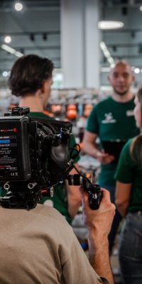 Cadreur filmant une équipe en magasin Maxi Zoo, devant des rayons d’accessoires pour animaux.